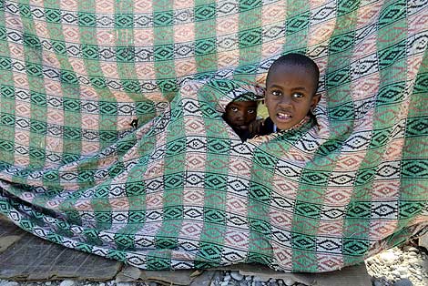 Dos niños se asoman al agujero de una manta. | Reuters