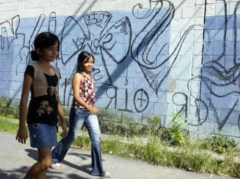 Dos jovenes caminan frente a dibujos de las maras en las calles de Paraso. | L. Bergamin