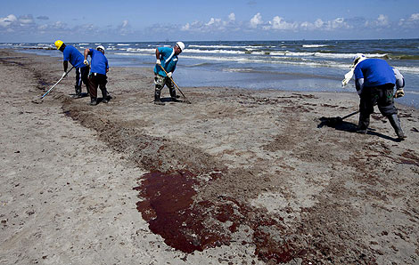 Operarios limpian los restos de crudo en la costa. | Efe