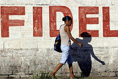 Una mujer camina delante de una pintada con el nombre del dictador. | Reuters