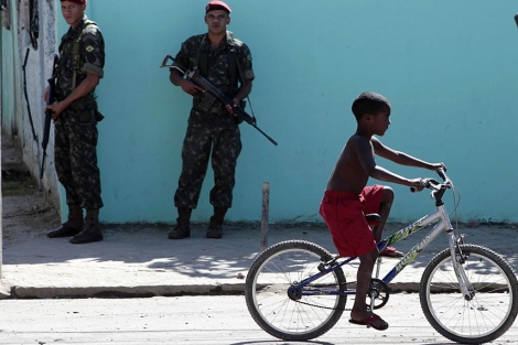 Un niño pasea en bicicleta junto a dos militares en Ciudad de Dios. | Reuters