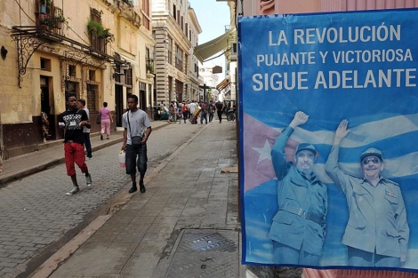 Varias personas caminan por una calle de La Habana junto a un cartel de los Castro. | Efe