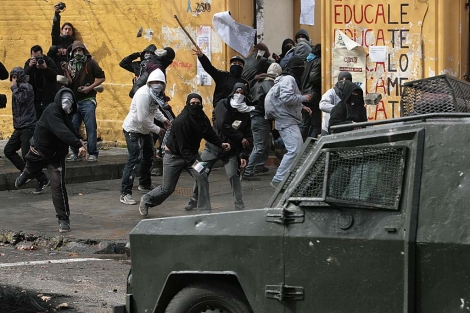 Jvenes encapuchados lanzan piedras contra un carro blindado de los Carabineros. | AP