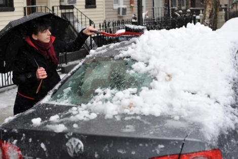 Una neoyorquina quita la capa de nieve caída sobre su coche. | Efe