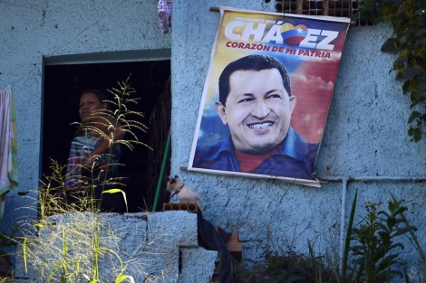 Una vecina de Caracas junto a un poster de Chávez. | Afp