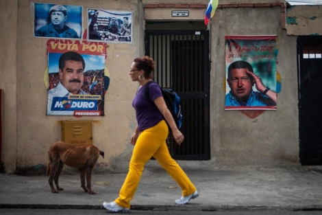 Una mujer camina frente a una casa con carteles de Chávez y Maduro. | Efe