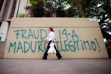 Una mujer camina frente a una pared con un mensaje de fraude electoral. | Efe