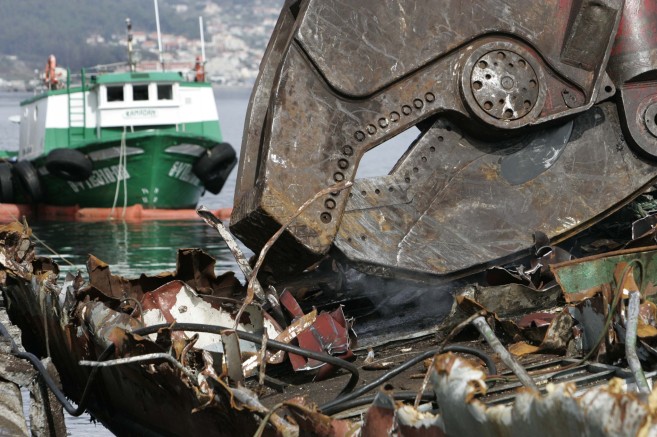 Una cizalla mecánica muerde los restos de un barco en el puerto de...