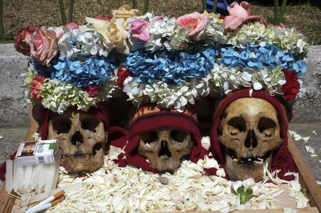 Tres calaveras adornadas con gorros y flores en el cementerio de La...