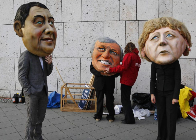 Activistas llevan mscaras de Angela Merkel (dcha.) y del lder...