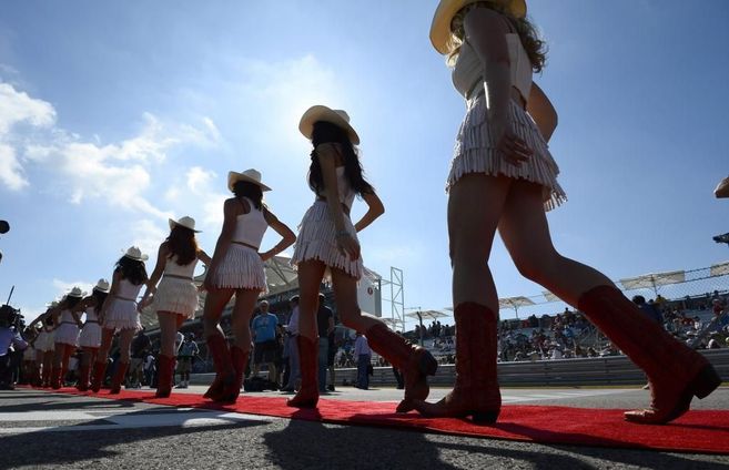 Un grupo de chicas desfilan ante de una carrera de coches.