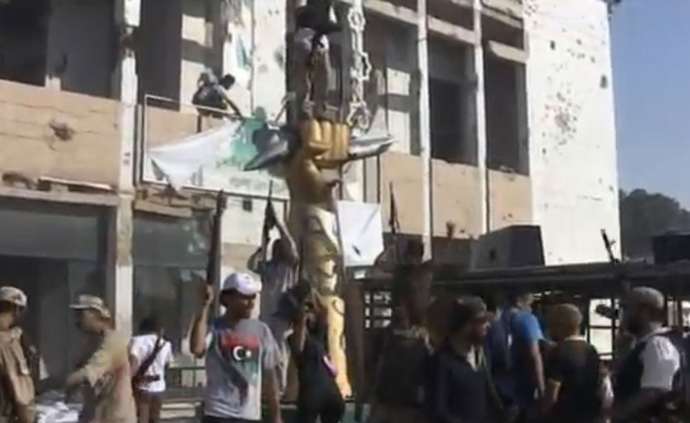 Rebeldes libios posan delante de una estatua encargada por Gadafi tras la toma de su palacio presidencial.
