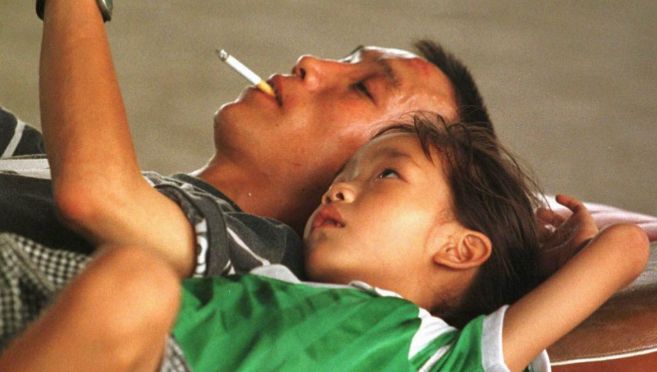 Un hombre chino fuma un cigarrillo mientras juega con su hijo.