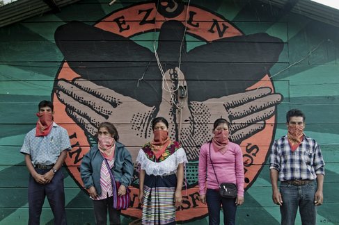Un grupo de zapatistas posa delante de un mural de Gram Om.