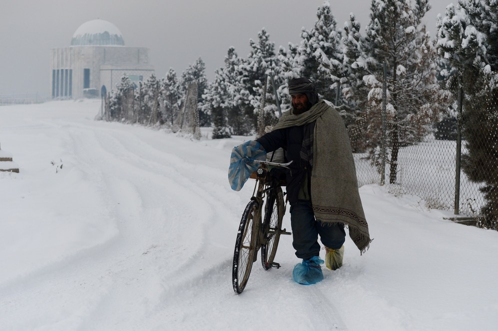 Un residente empuja su bicicleta por una carretera cubierta de nieve...