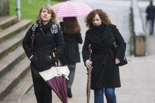 Dos mujeres jvenes caminan con paraguas cerrados, una al lado de...