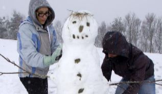 Un hombre y una mujer estn acabando de formar un mueco de nieve,...