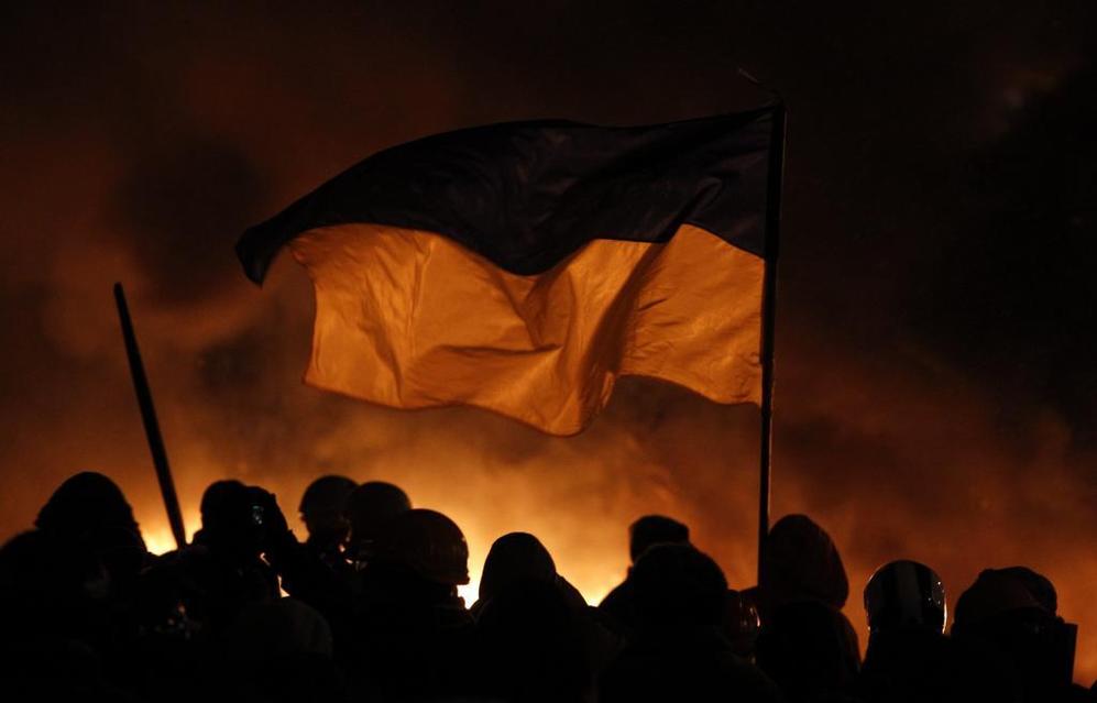 Varios manifestantes sujetan la bandera de Ucrania. Al fondo, una nube...