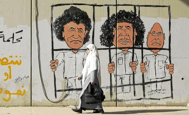 Una mujer camina por una calle de Trpoli junto a un mural que...