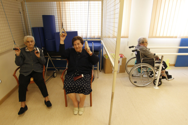 Dos personas mayores realizan ejercicios terapéuticos en una...