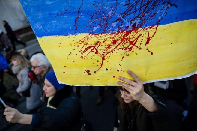 Una mujer sostiene una bandera ucraniana manchada de sangre,