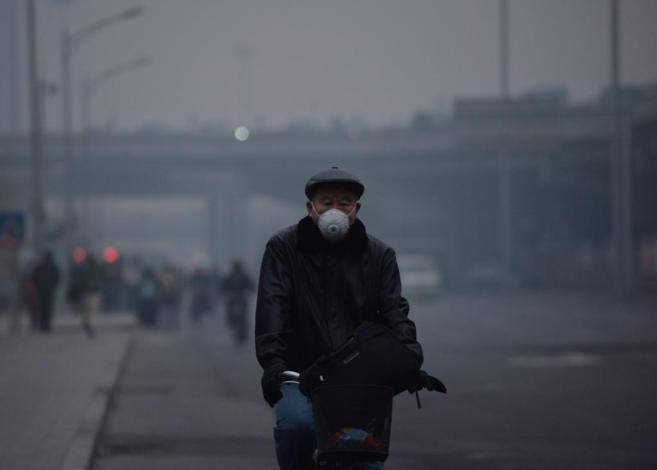 Un hombre con mascarilla mientras pedalea en Beijing.