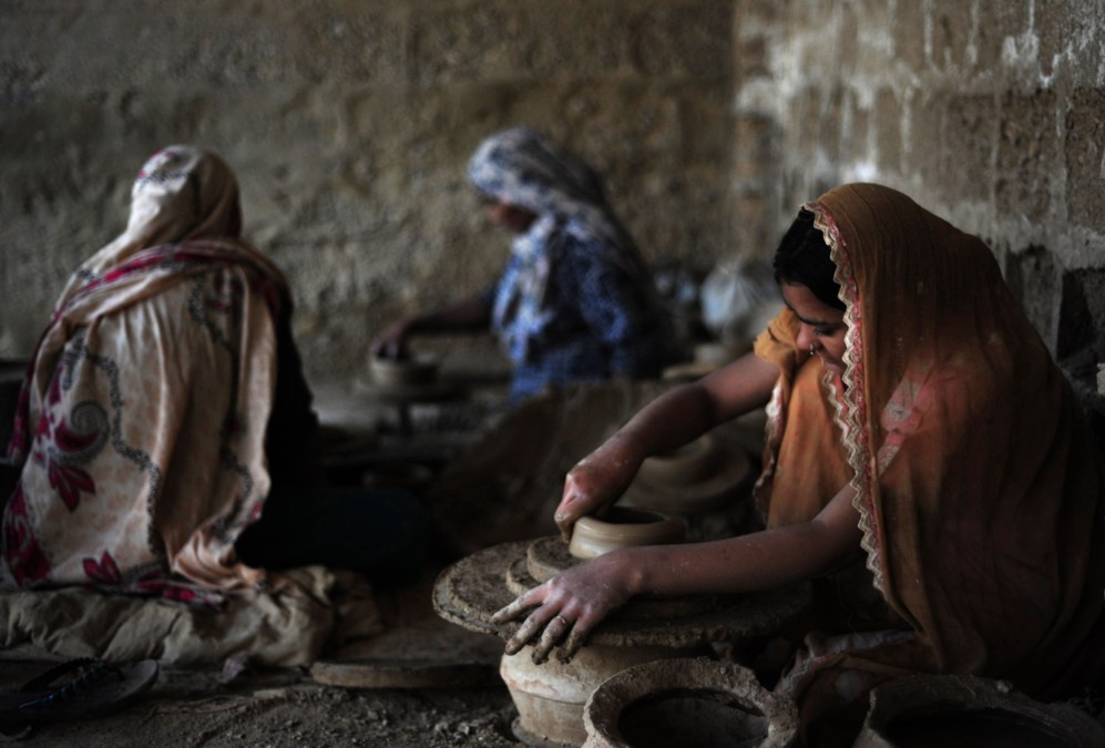 Un artesano paquistan hace ollas de barro junto a sus hijas en su...