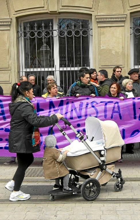 Una mujer pasea un carrito junto a una protesta feminista.