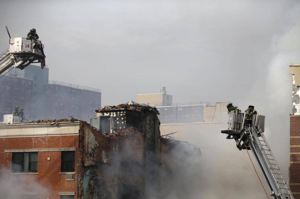 Los bomberos tratan de extinguir el fuego en el techo de los edificios...