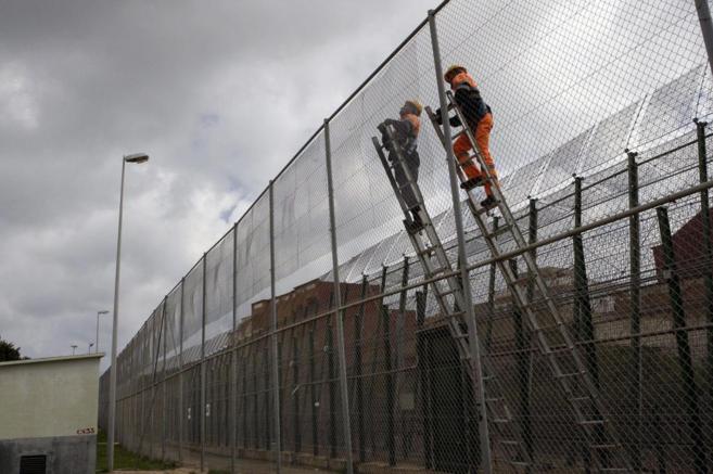 Dos hombres refuerzan la valla fronteriza en Melilla.