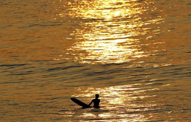 Un surfista en el agua, con su tabla en el mar. El agua está naranjo...