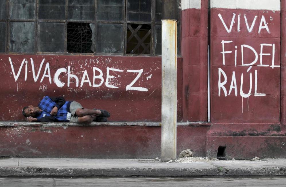 Un hombre duerme en un poyete, en La Habana, bajo un grafiti de apoyo...