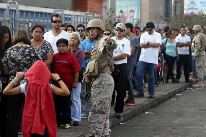 Un militar chileno da instrucciones a varias personas que hacen cola...