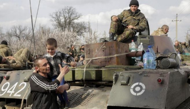 Un hombre juega con su hijo junto a soldados ucranianos en las afueras...