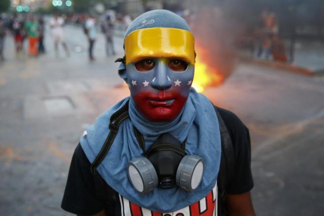 Un joven durante las protestas con una mascara con los colores de la...