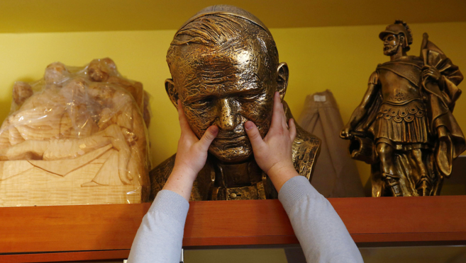 Un vendedor saca un busto de Juan Pablo II de la estantera de una...