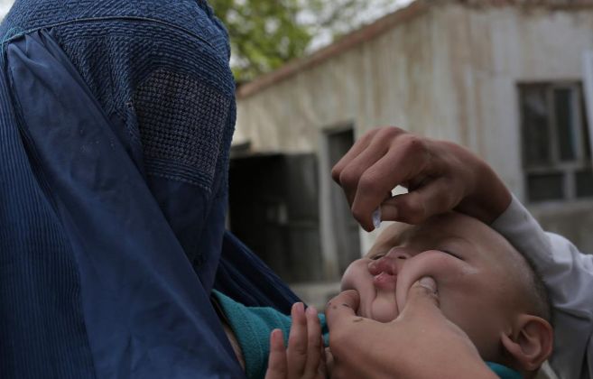 Un nio recibe la vacuna de la polio en brazos de su madre, cubierta...