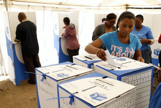 Una mujer introduce su voto en una urna en un colegio electoral de...
