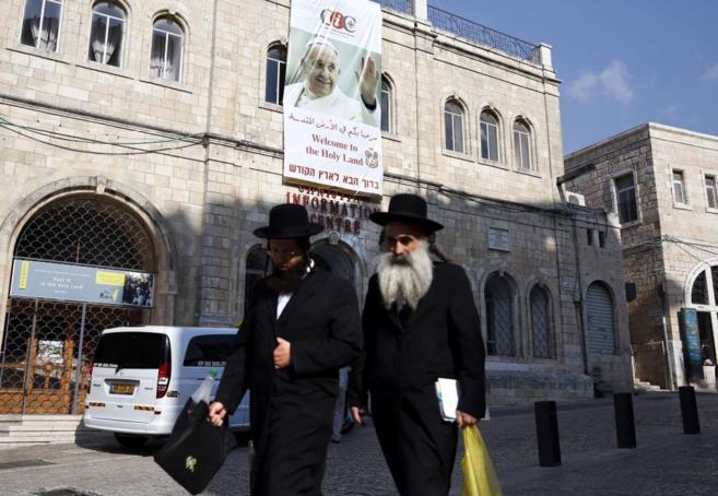 Dos judíos ultraortodoxos caminan por delante de un cartel del Papa...