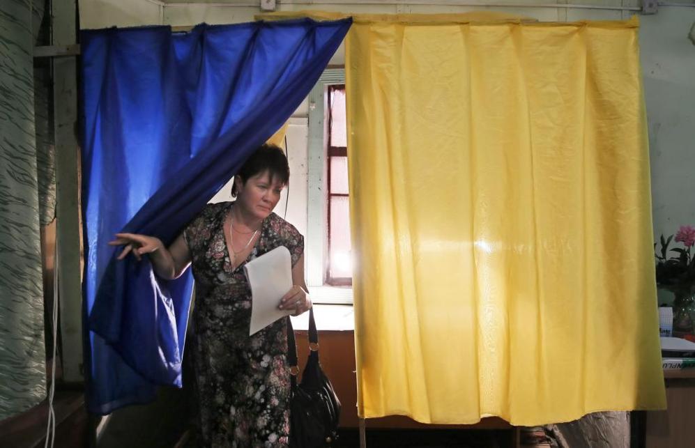 Una mujer sale de una cabina de votacin, con cortinas que forman la...