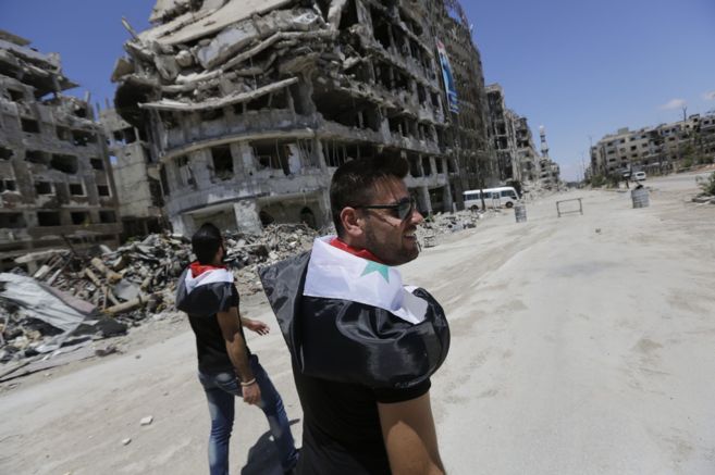 Sirios caminan entre los escombros de edificios destruidos en Homs.