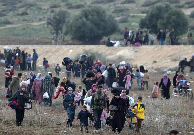 Decenas de refugiados sirios cruzan campo a través cargados con sus...