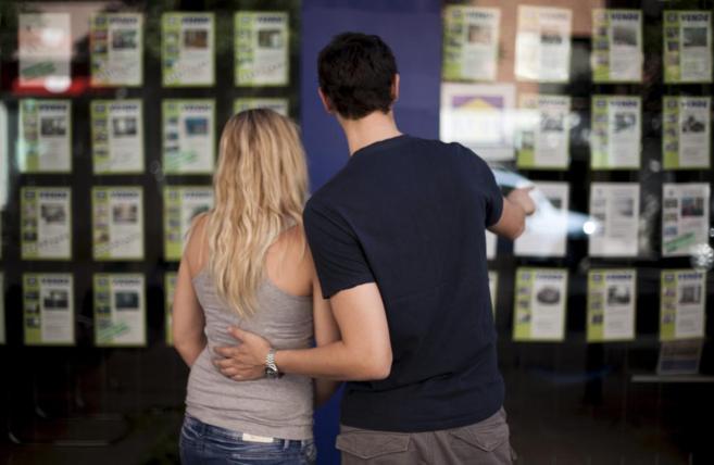 Una pareja mira anuncios de viviendas en venta en el escaparate de una...