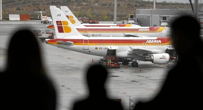 Un grupo de pasajeros observa aviones de Iberia en la terminal 4 del...