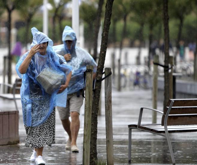 Dos turistas intentan protegerse con chubasqueros de una tormenta en...
