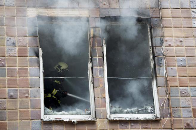 Un bombero apaga el fuego de la vivienda incendiada.