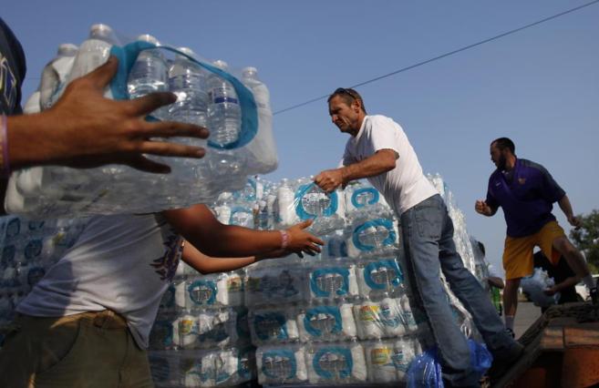 Algunos voluntarios descargan botellas de agua de un camión en...
