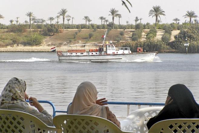 Unas mujeres ven pasar un barco por el Canal de Suez en la ciudad de...