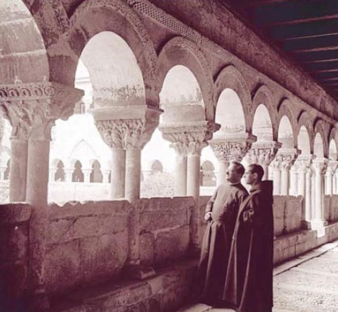 Dos monjes contemplan desde el interior de la arcada el claustro...