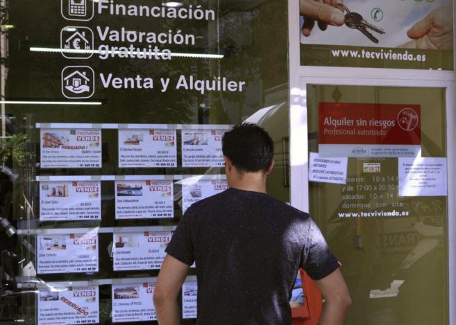 Un joven mira el escaparate de una inmobiliaria en Madrid con anuncios...